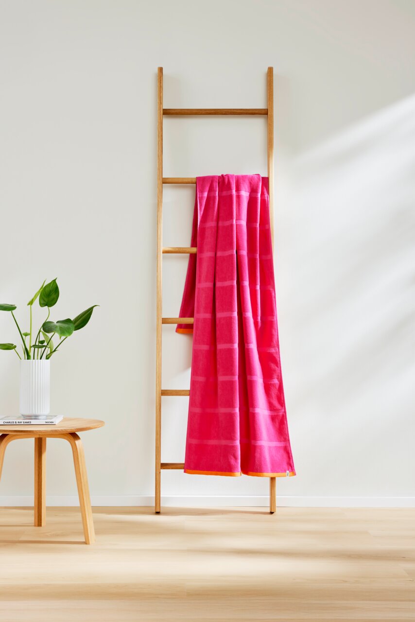 s.Oliver Strandtuch Ein pinkfarbenes Strandtuch mit Karomuster hängt über einer Holzleiter, seitliche Perspektive.