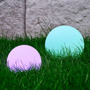 Zwei kugelförmige Solarleuchten von Ambia Garden im Gras, eine in Lila und eine in Türkis, aus seitlicher Perspektive fotografiert.