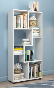 Weißes, modernes Bücherregal mit asymmetrischen Fächern, gefüllt mit Büchern und Dekoration, freistehend vor blauer Wand, Frontansicht leicht schräg von vorn.