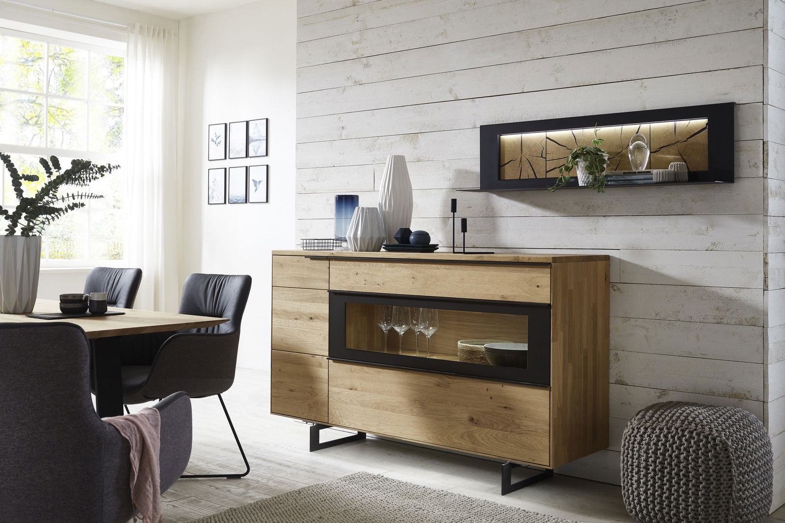 Modernes Wohnzimmer mit einem hölzernen Wandboard an einer weißen Wand, dekoriert mit Pflanzen und Kunstobjekten, seitliche Perspektive.