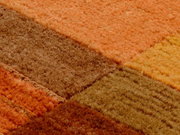 Nahaufnahme eines Wollteppichs mit quadratischem Muster in warmen Erdtönen wie Orange, Braun und Gelb.