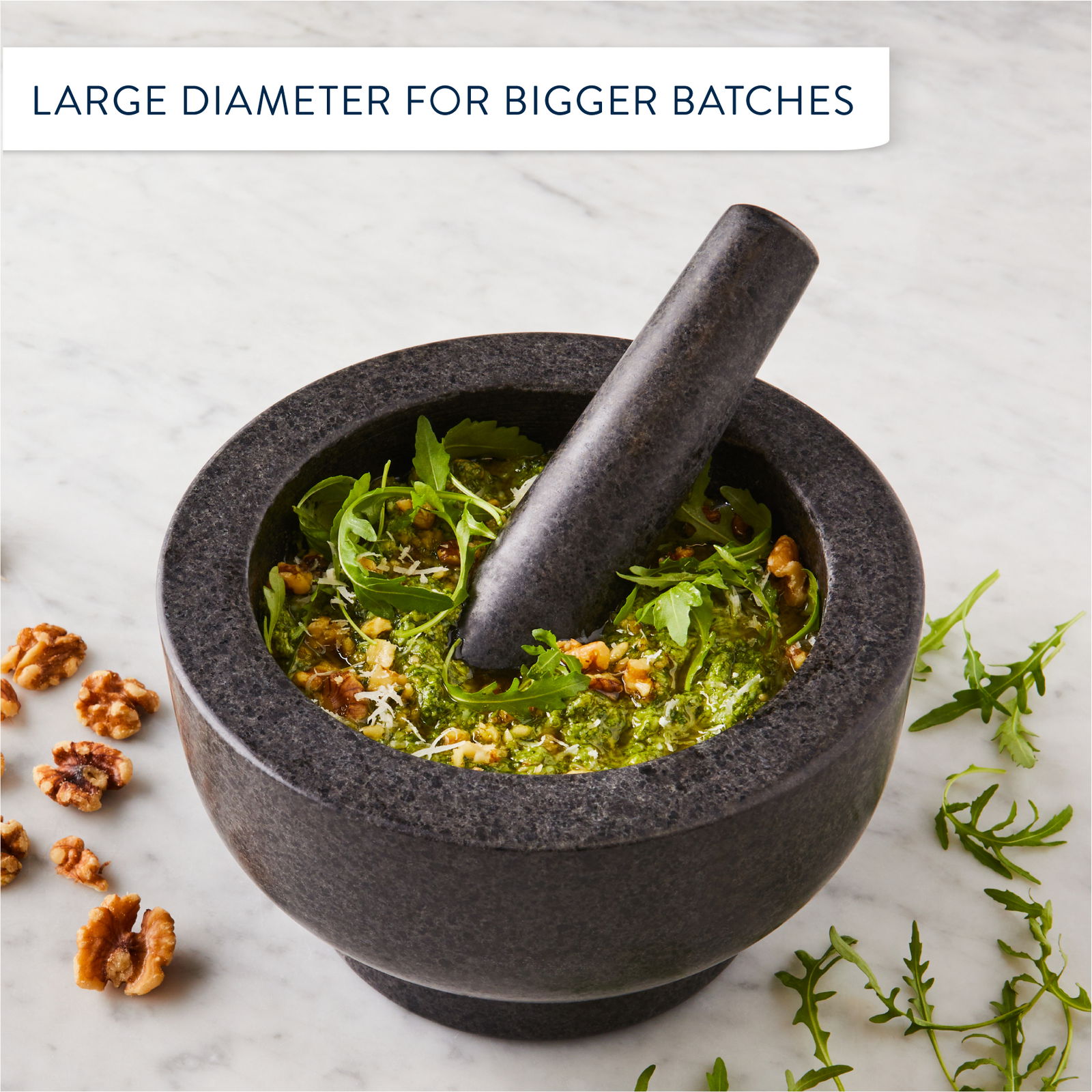 Mörser und Stößel aus dunklem Stein, gefüllt mit Pesto und Rucola, aus der Vogelperspektive fotografiert.