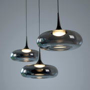 Drei moderne Pendelleuchten aus getöntem Glas mit warmweißem Licht, in leicht seitlicher Ansicht von unten vor grauem Hintergrund