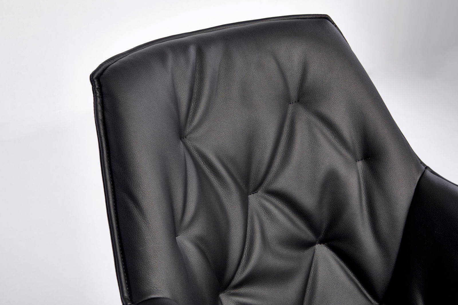Nahaufnahme der Rückenlehne eines schwarzen Bürostuhls mit gepolstertem Lederbezug und Steppnähten.