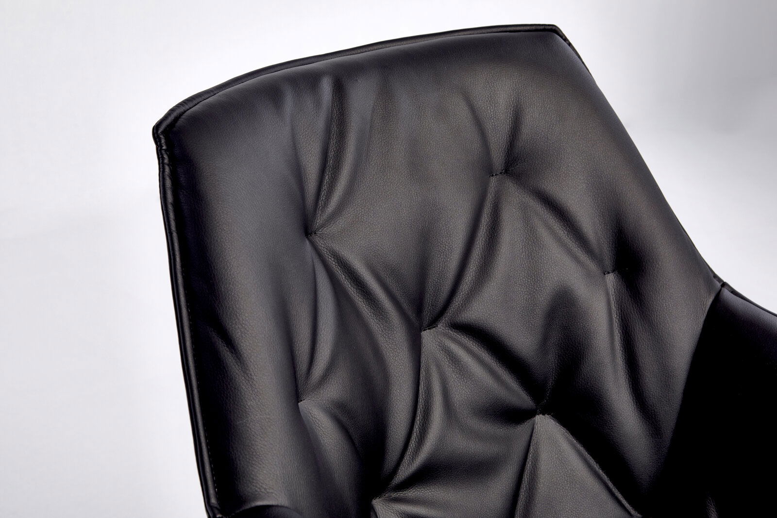 Nahaufnahme der Rückenlehne eines schwarzen Bürostuhls mit gepolstertem Lederbezug und Steppnähten.