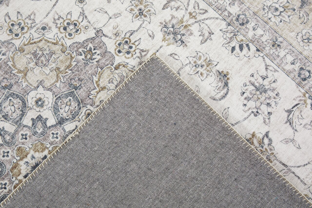 Close-up van een tapijt met een bloemmotief in beige- en grijstinten, gedeeltelijk omgeslagen om de achterkant te laten zien.