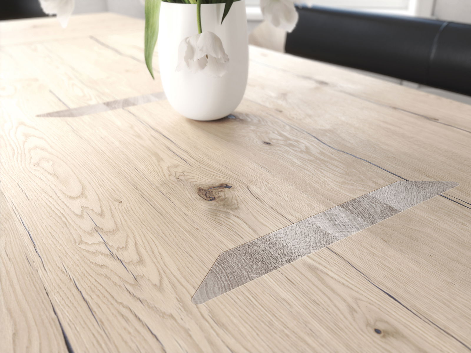 Nahaufnahme eines Voglauer Esstisches V-ROCK aus hellem Holz mit natürlicher Maserung und dekorativen Einlagen, darauf steht eine weiße Vase mit Blumen. Perspektive von schräg oben.
