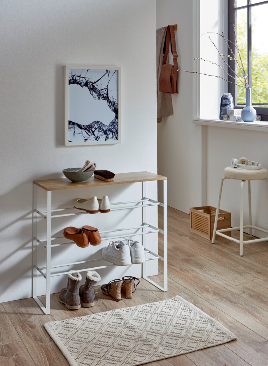 Modernes Schuhregal mit weißem Metallgestell und Holzablage im Flur, mit mehreren Paar Schuhen bestückt; Perspektive: frontale Ansicht leicht von links in einem hellen Raum am Fenster.