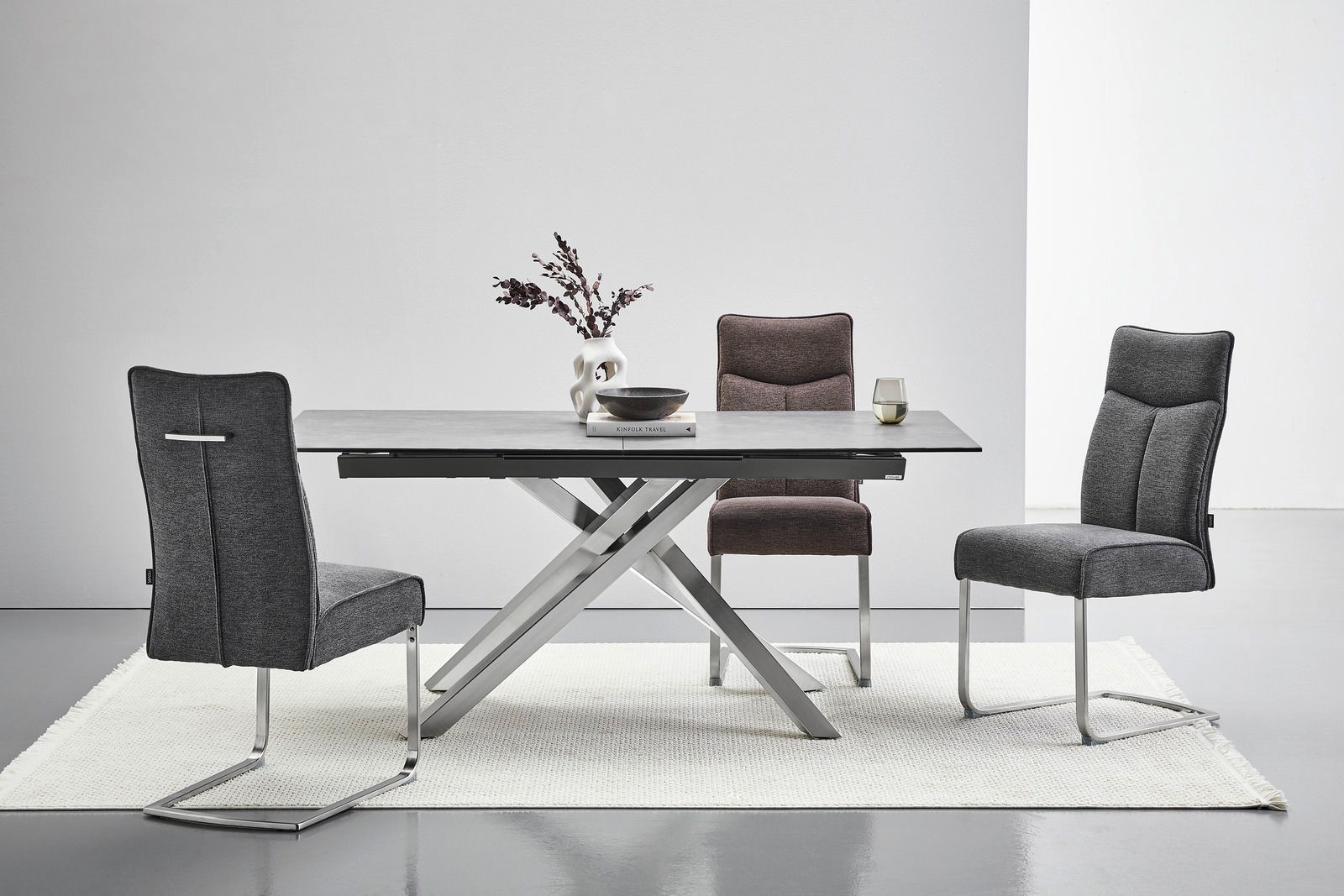 Moderner Essbereich mit einem rechteckigen Tisch und drei Freischwinger-Stühlen in verschiedenen Grautönen, seitliche Perspektive.