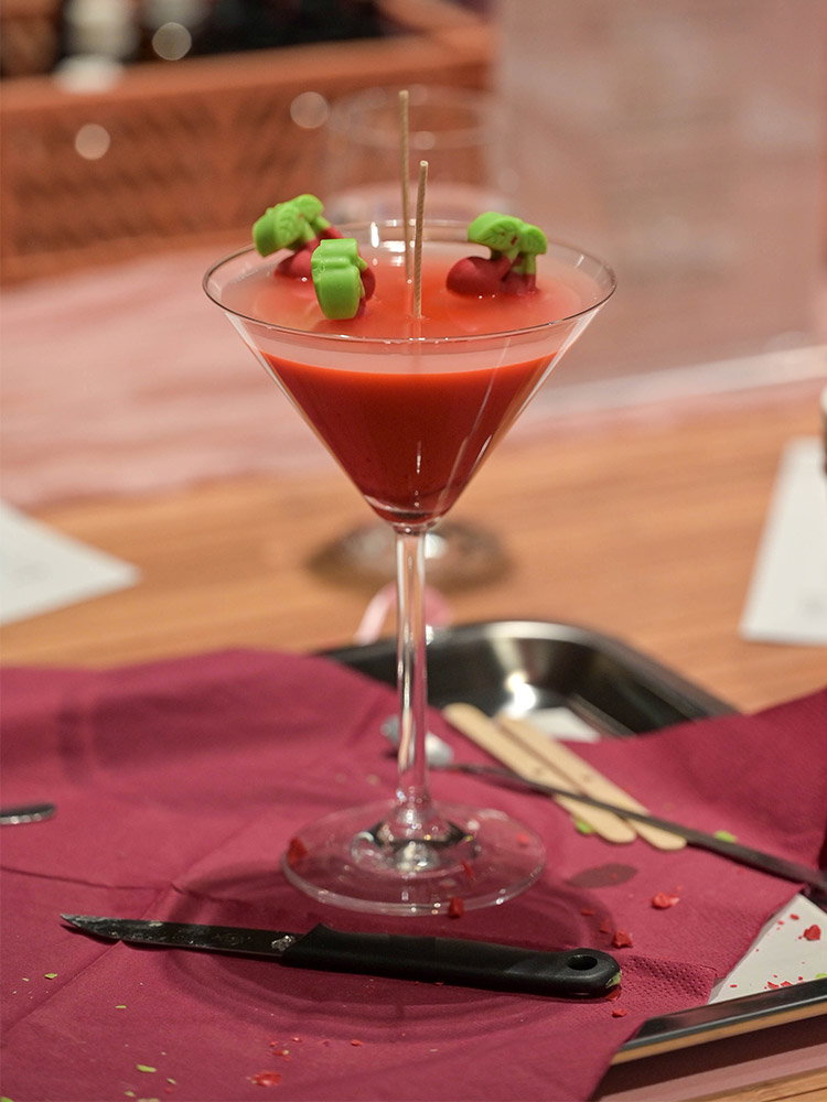Zelfgemaakte rode kaars in een cocktailglas, versierd met decoratief fruit als origineel DIY-project.