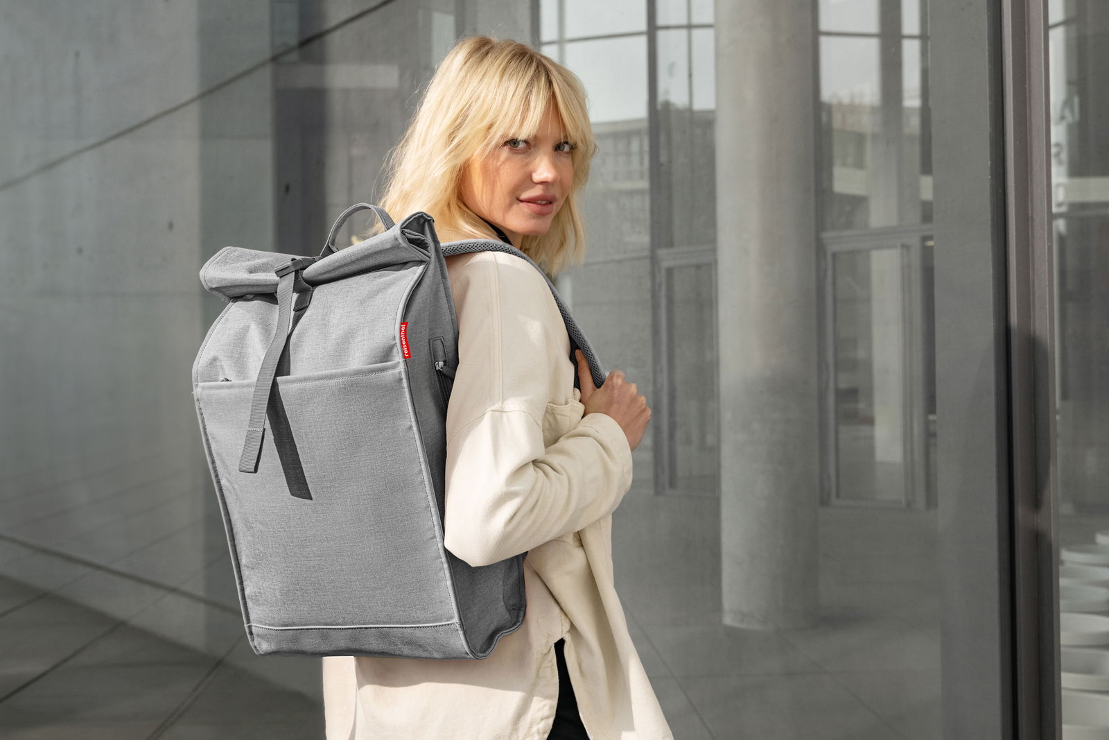 Frau mit grauem urbanem Rolltop-Rucksack von hinten in städtischer Umgebung