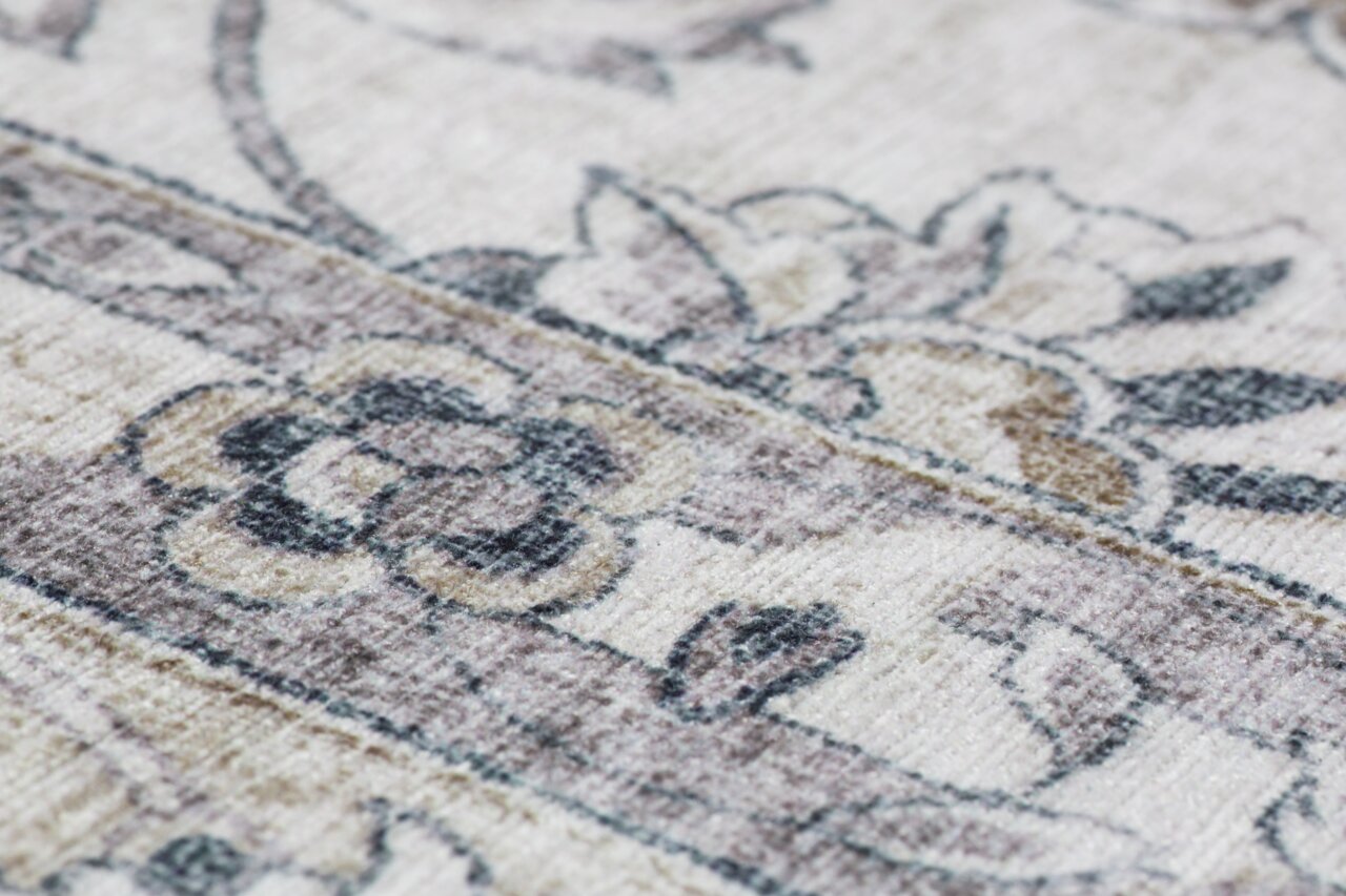 Nahaufnahme eines Teppichs mit floralem Muster in sanften Beige- und Grautönen, schräg von der Seite fotografiert.