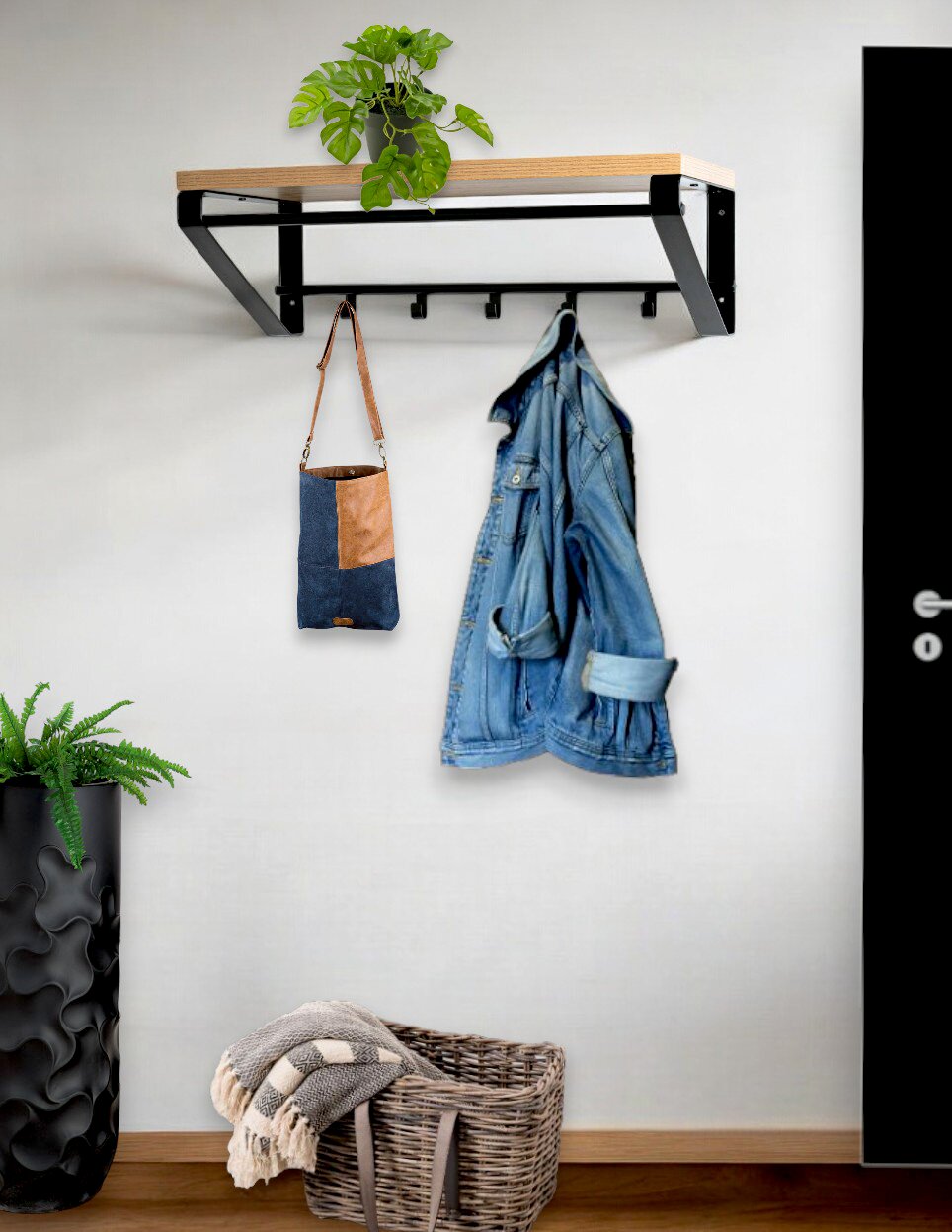 Wandgarderobe mit schwarzem Metallrahmen und Holzablage, darunter mehrere Haken, mit aufgehängter Tasche und Jeansjacke; Perspektive: frontale Ansicht leicht von links