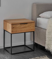 Moderne Nachtkommode aus Holz mit schwarzem Metallgestell, seitliche Perspektive neben einem Bett.