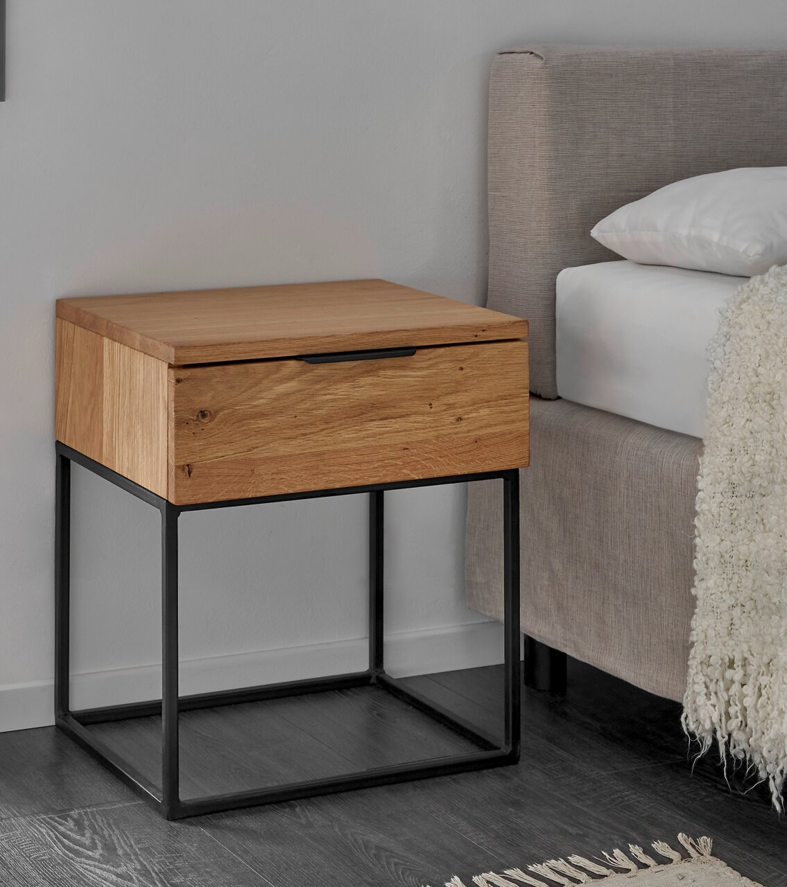 Moderne Nachtkommode aus Holz mit schwarzem Metallgestell, seitliche Perspektive neben einem Bett.