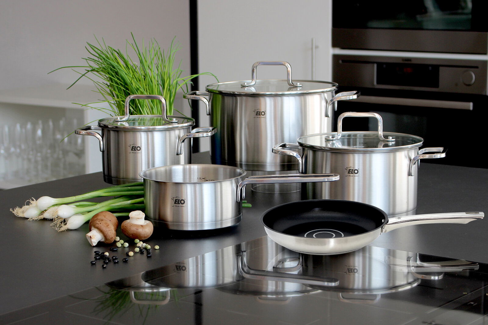 Topfset Topas 5-tlg. aus Edelstahl, bestehend aus vier Töpfen mit Glasdeckeln und einer Pfanne, auf einer Küchenarbeitsplatte präsentiert. Perspektive von vorne.
