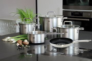 Topfset Topas 5-tlg. aus Edelstahl, bestehend aus vier Töpfen mit Glasdeckeln und einer Pfanne, auf einer Küchenarbeitsplatte präsentiert. Perspektive von vorne.