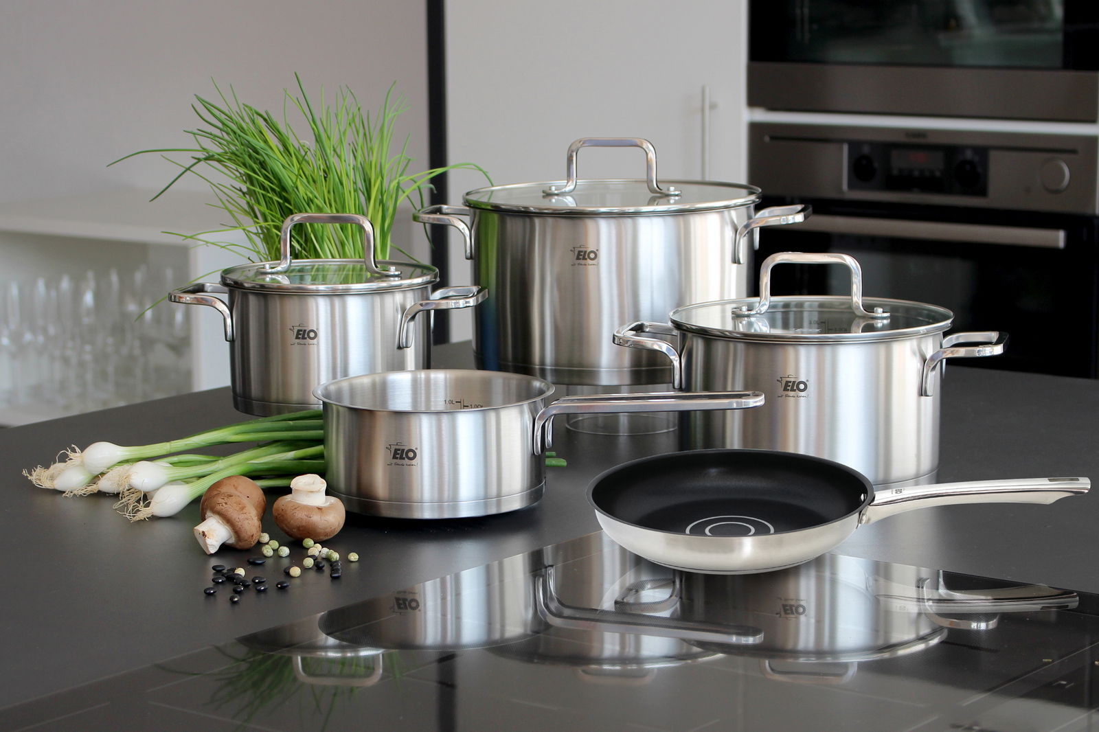 Topfset Topas 5-tlg. aus Edelstahl, bestehend aus vier Töpfen mit Glasdeckeln und einer Pfanne, auf einer Küchenarbeitsplatte präsentiert. Perspektive von vorne.