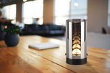 Moderne LED-Tischleuchte in zylindrischer Form auf einem Holztisch, seitliche Perspektive.