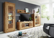 Wohnzimmeransicht mit der Landscape Wandkombination MERAN in natürlichem Holzdesign, bestehend aus einem hohen Schrank, einem TV-Board und einem Vitrinenschrank, mit dekorativen Elementen und Pflanzen, seitliche Perspektive.