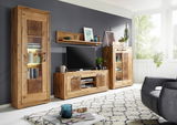Wohnzimmeransicht mit der Landscape Wandkombination MERAN in natürlichem Holzdesign, bestehend aus einem hohen Schrank, einem TV-Board und einem Vitrinenschrank, mit dekorativen Elementen und Pflanzen, seitliche Perspektive.