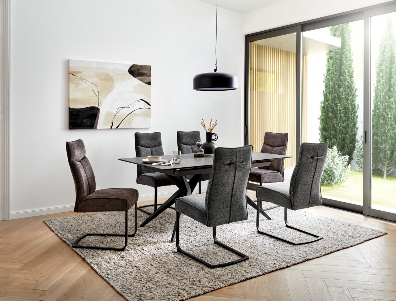 Moderner Esstisch mit sechs gepolsterten Stühlen in einem hellen Raum mit großen Fenstern, seitliche Perspektive.