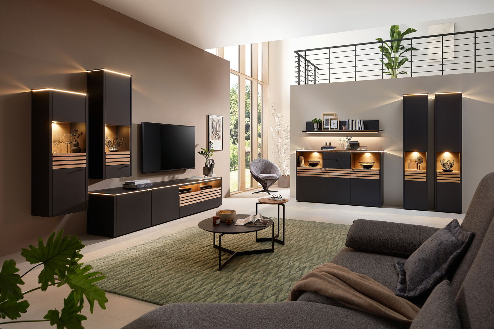 Moderne Wohnzimmer-Wandkombination in dunklen Tönen mit integrierter Beleuchtung, bestehend aus Hängeschränken, TV-Board und Vitrine, aus der Perspektive eines gemütlichen Wohnzimmers mit Sofa und Teppich.