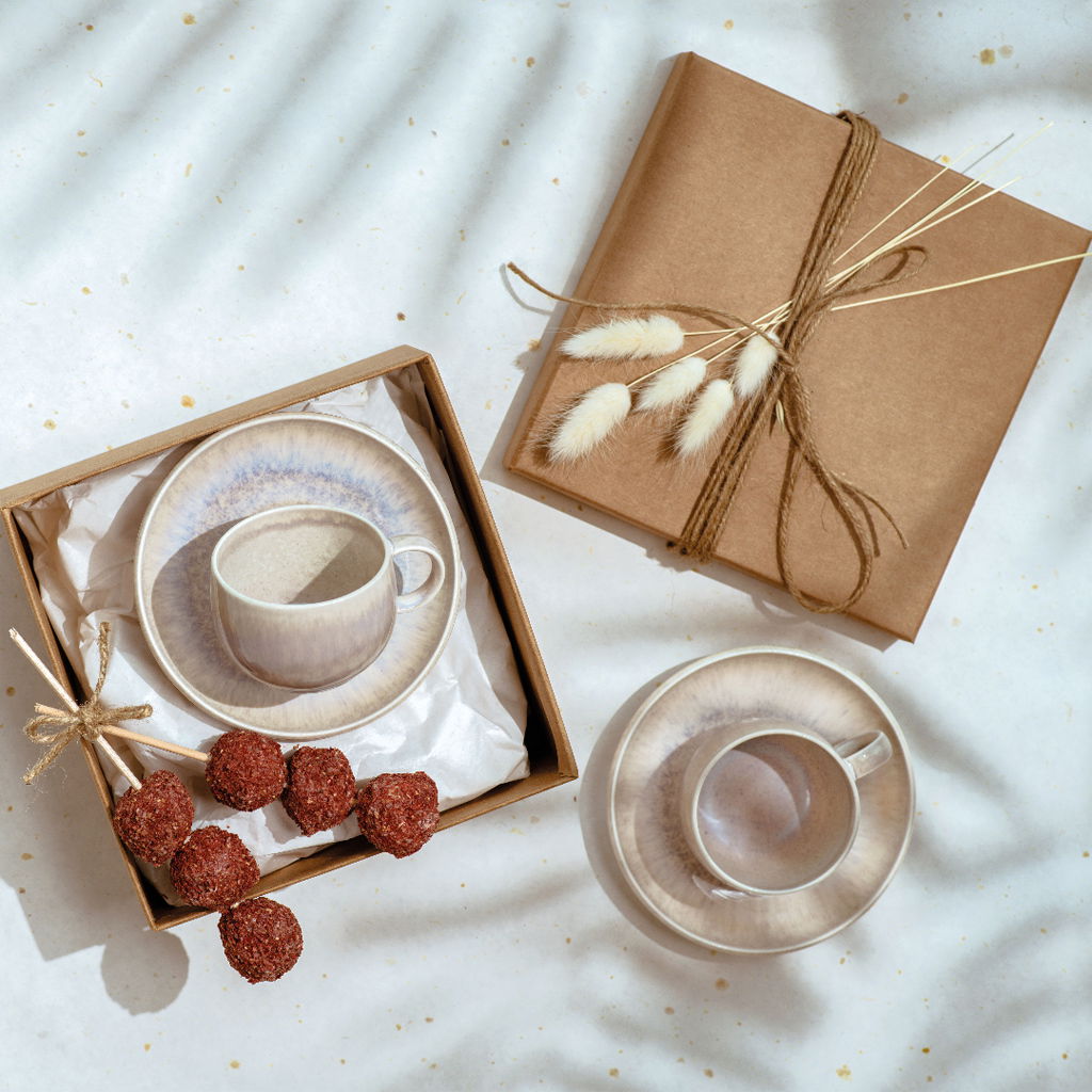 Espressotasse mit Untertasse in Geschenkbox, von oben fotografiert, neben Geschenkverpackung und Schokoladenpralinen auf einem hellen Hintergrund.
