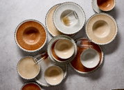 Bovenaanzicht van een stijlvol servies met borden, kommen en glazen in warme aardetinten en grijs, afgewerkt met verfijnde zwarte streepjes langs de randen.