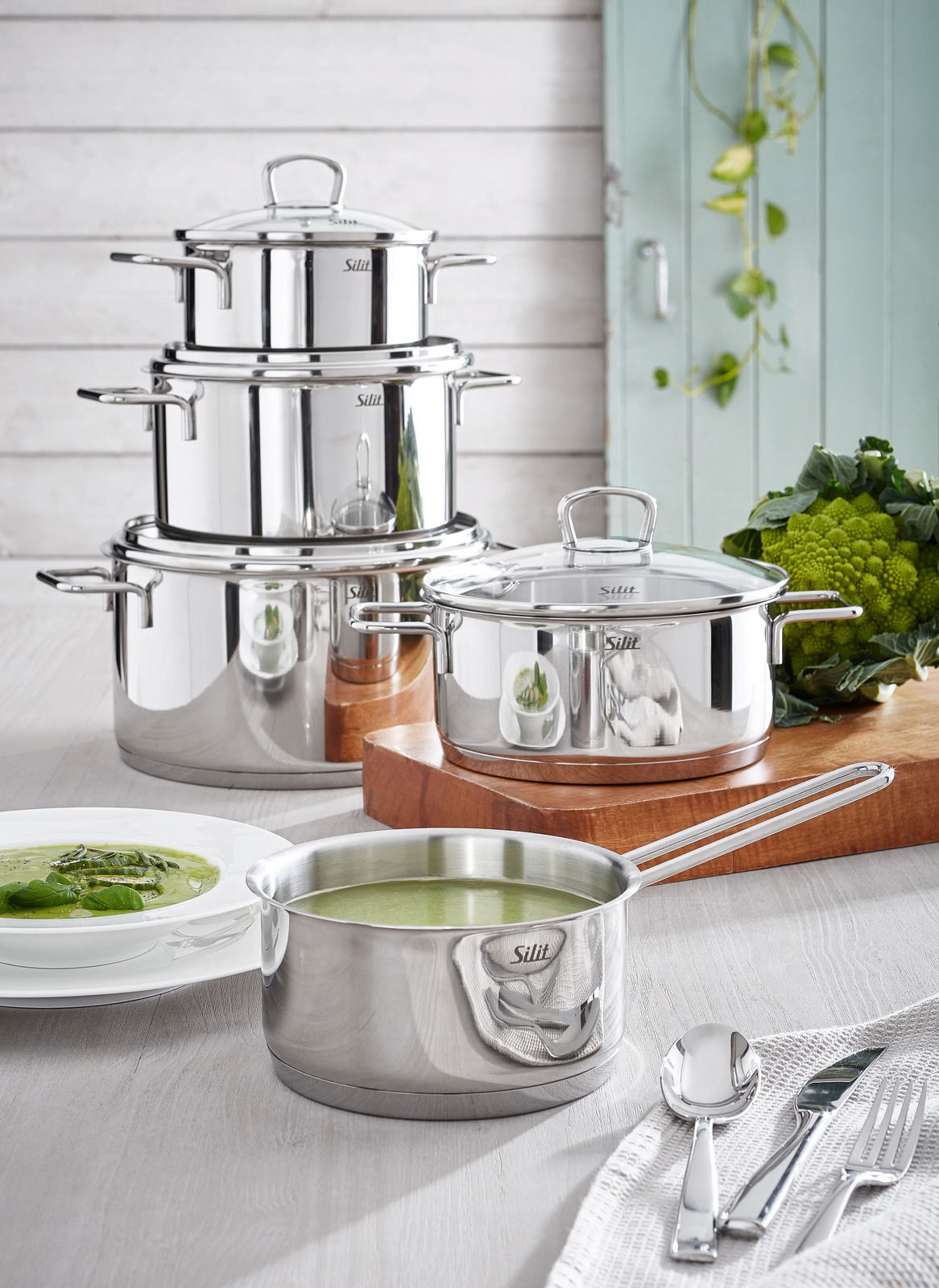 Das Topfset Alicante 5-tlg aus Edelstahl, bestehend aus mehreren Töpfen und einer Kasserolle, präsentiert in einer modernen Küchenumgebung mit frischem Gemüse. Perspektive: seitlich von vorne.