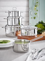 Das Topfset Alicante 5-tlg aus Edelstahl, bestehend aus mehreren Töpfen und einer Kasserolle, präsentiert in einer modernen Küchenumgebung mit frischem Gemüse. Perspektive: seitlich von vorne.