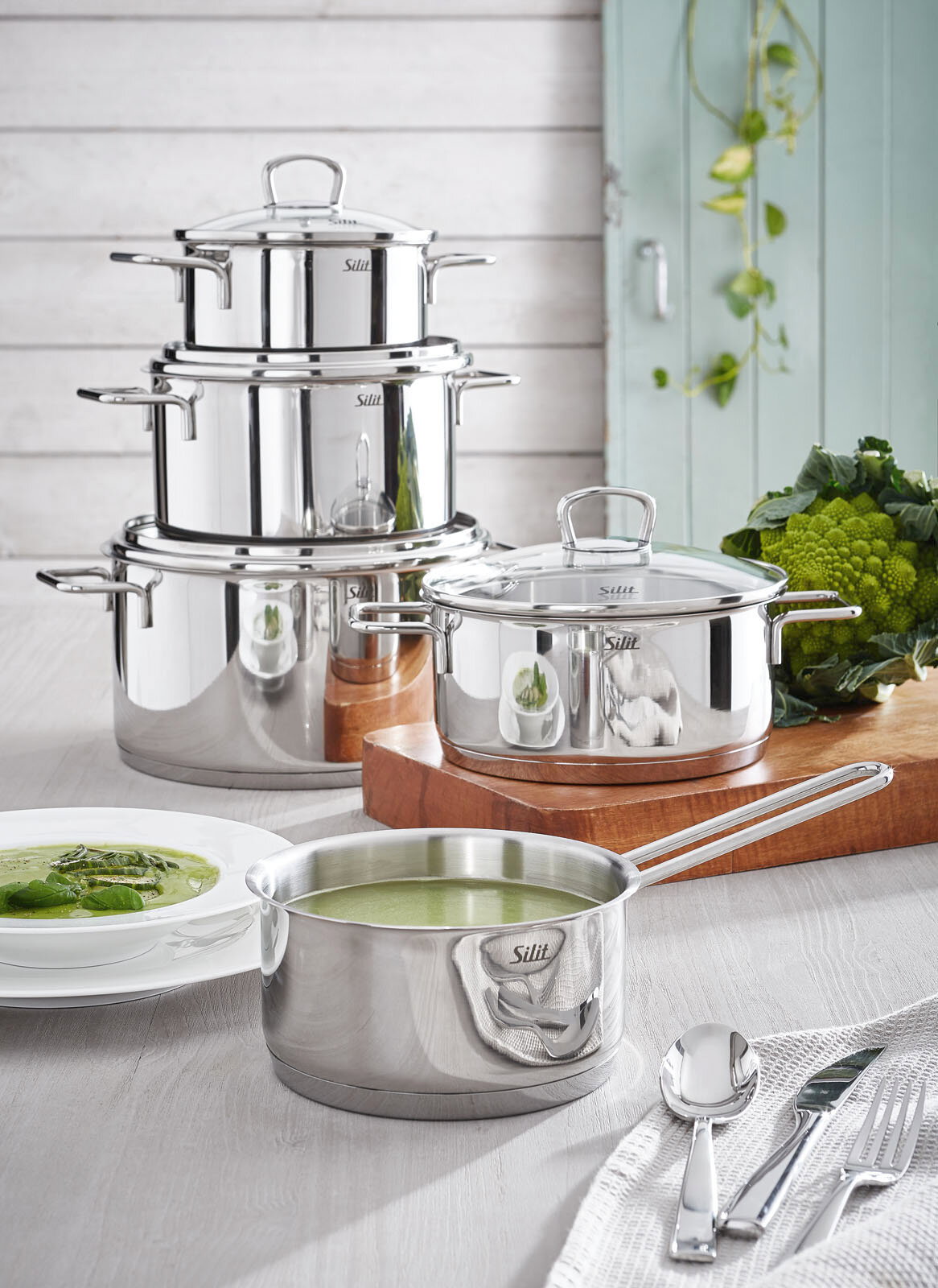 Das Topfset Alicante 5-tlg aus Edelstahl, bestehend aus mehreren Töpfen und einer Kasserolle, präsentiert in einer modernen Küchenumgebung mit frischem Gemüse. Perspektive: seitlich von vorne.