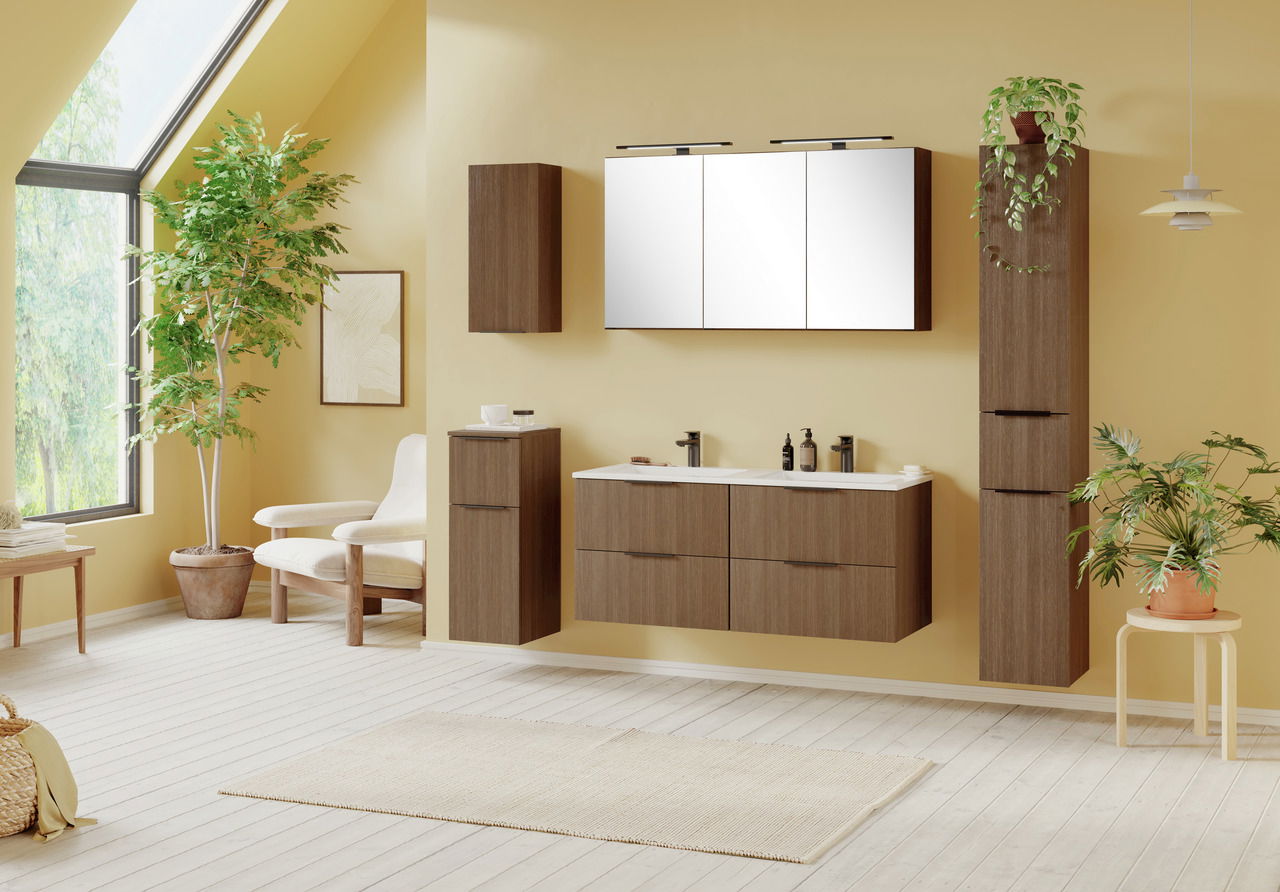 Moderner Badezimmer-Unterschrank in Holzoptik, frontal betrachtet, mit zwei Waschbecken und Stauraum darunter, umgeben von Pflanzen und heller Einrichtung.