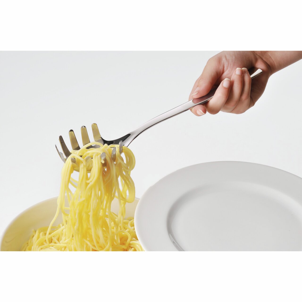 Hand hält einen glänzenden Nudellöffel, der Spaghetti aus einer Schüssel hebt, seitliche Perspektive.