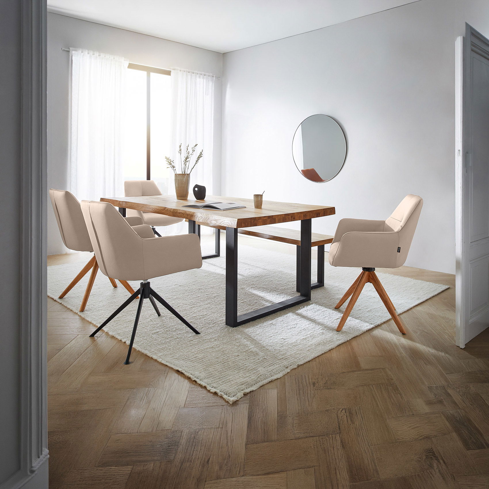 Helles Esszimmer mit Holztisch, vier beigen Drehstühlen, Teppich und rundem Wandspiegel