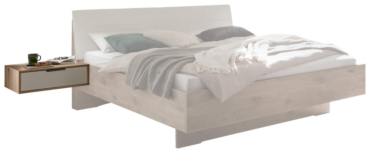 Modernes Holzbett in heller Eichenoptik mit gepolstertem, hellgrauem Kopfteil und schwebendem Nachttisch mit Schublade, dekoriert mit Bettwäsche und Decken; Ansicht schräg von vorn links.