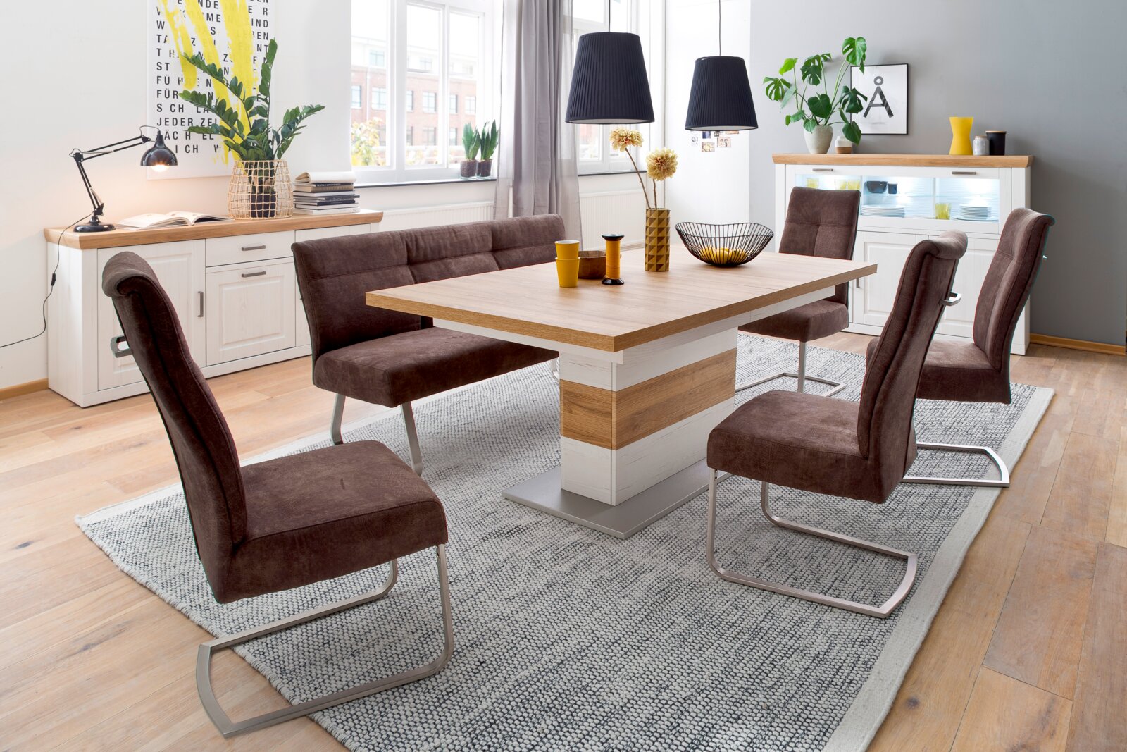 Modernes Esszimmer-Set mit rechteckigem Holztisch in Weiß/Eiche-Optik und vier braunen Freischwinger-Stühlen auf grauem Teppich, gezeigt in leicht erhöhter Perspektive schräg von vorn.
