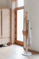 Moderner Garderobenständer aus Holz mit weißen Haken, von der Seite fotografiert, mit Mantel und Tasche behängt, in einem hellen Eingangsbereich.