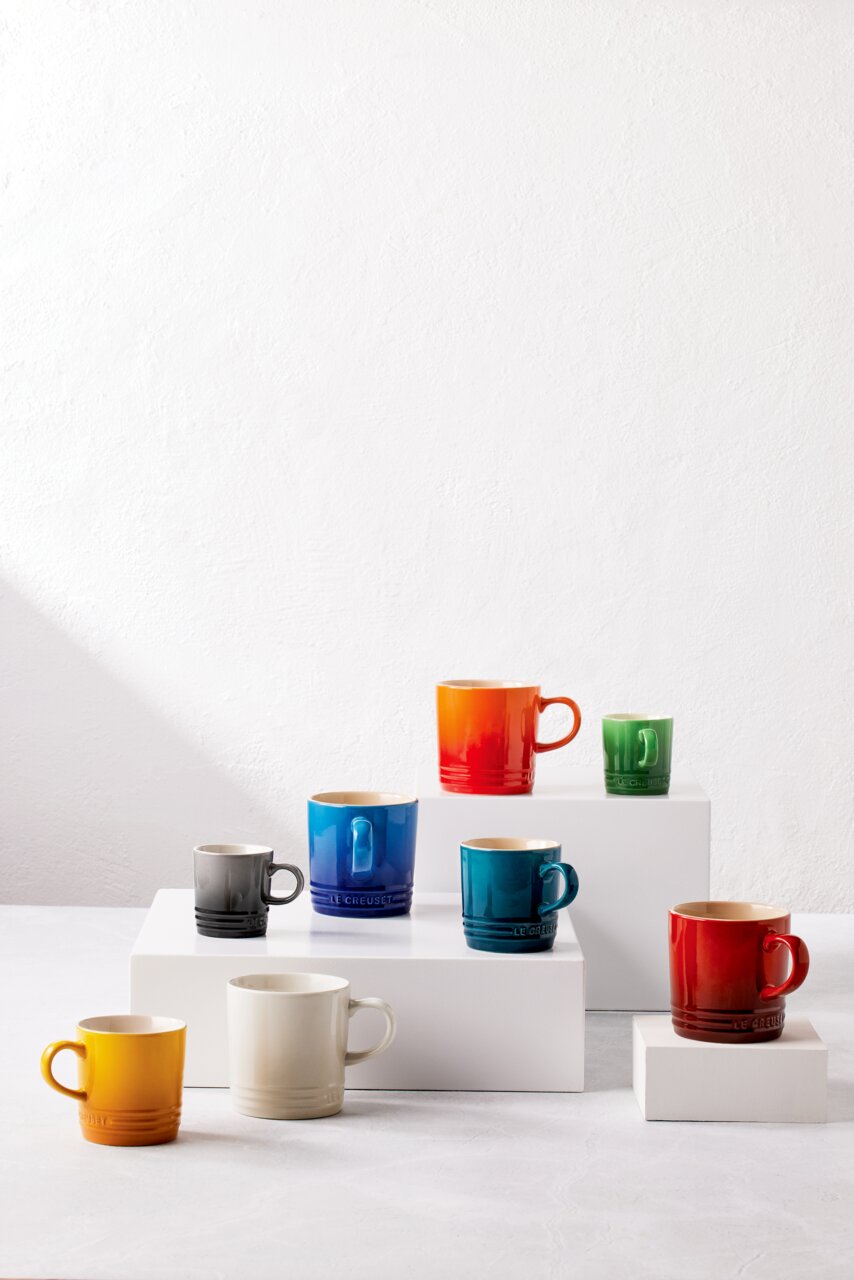 Verschiedene bunte Becher, darunter ein roter Becher, auf weißen Podesten aus einer leicht erhöhten Perspektive.