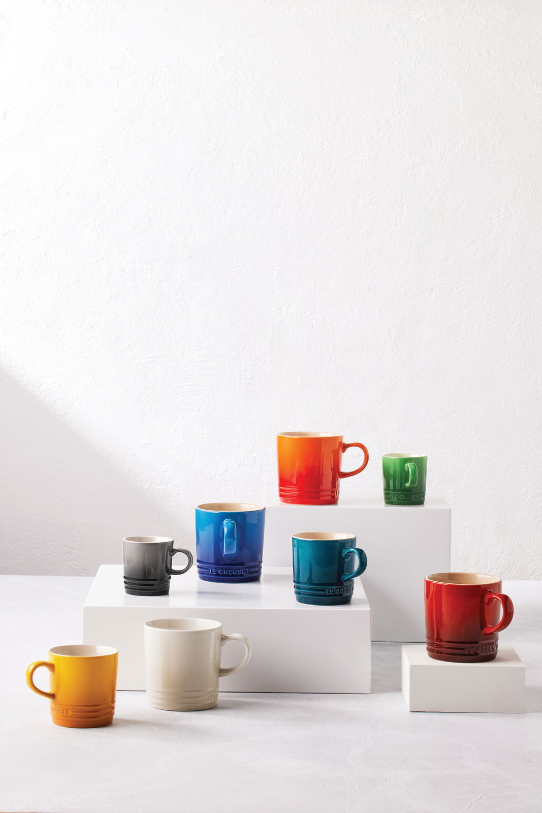 Verschiedene bunte Becher, darunter ein roter Becher, auf weißen Podesten aus einer leicht erhöhten Perspektive.