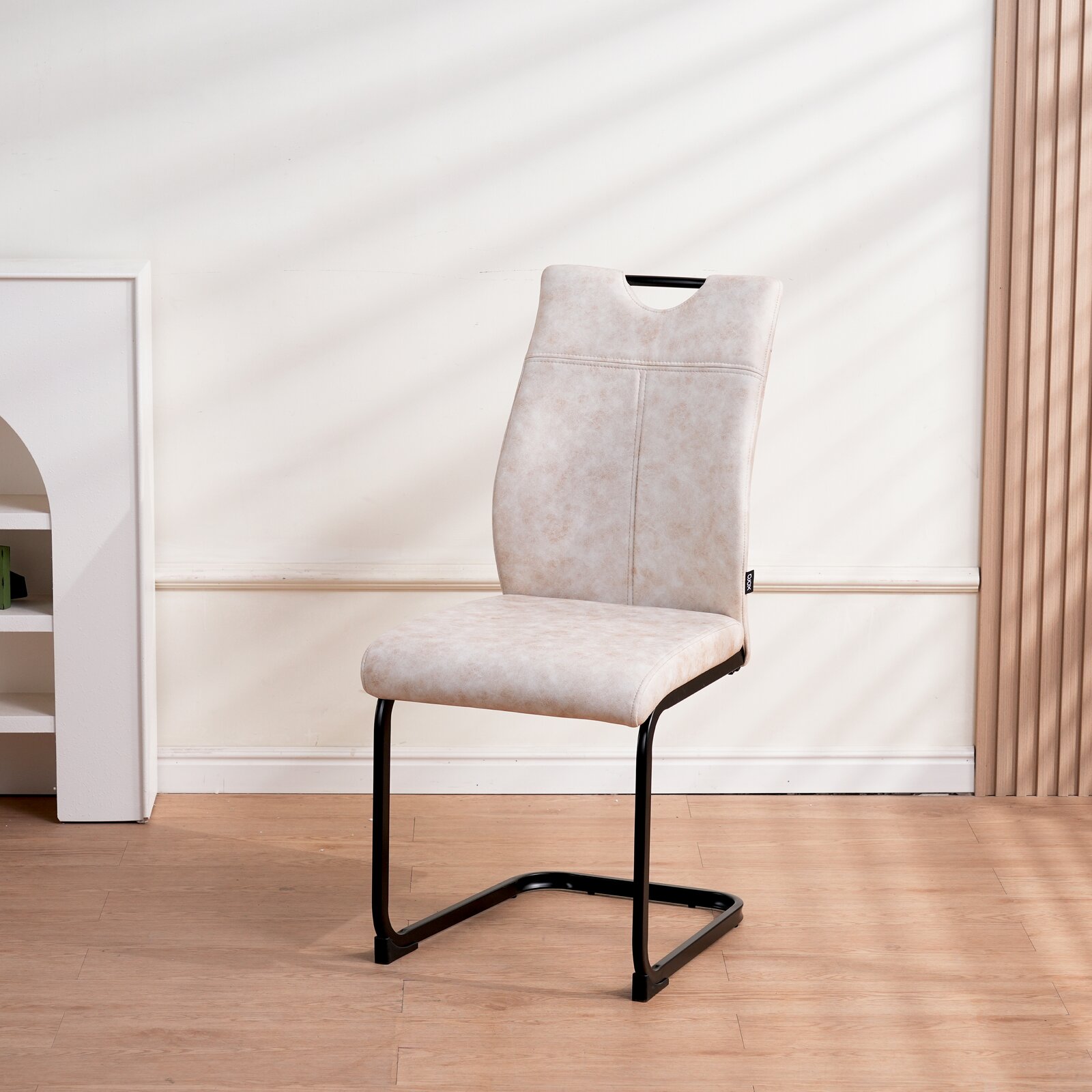 Moderner Schwingstuhl mit beigem Polster und schwarzem Metallgestell, seitliche Perspektive