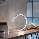 Moderne Tischleuchte MINI RITUS in Ringform auf einem Tisch, seitliche Perspektive, neben einem geöffneten Buch.