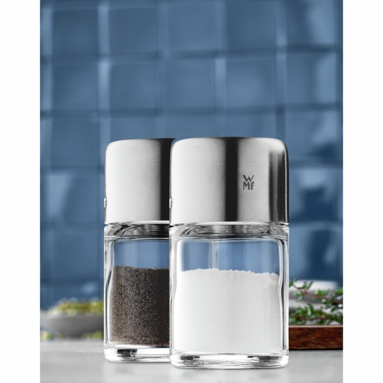 Salz- und Pfefferstreuer-Set BEL GUSTO aus Glas und Edelstahl, Vorderansicht vor blauem Hintergrund.