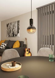 Moderne Pendelleuchte YORTH mit sichtbarem Glühfaden, hängend über einem Tisch in einem stilvoll eingerichteten Wohnzimmer, seitliche Perspektive.