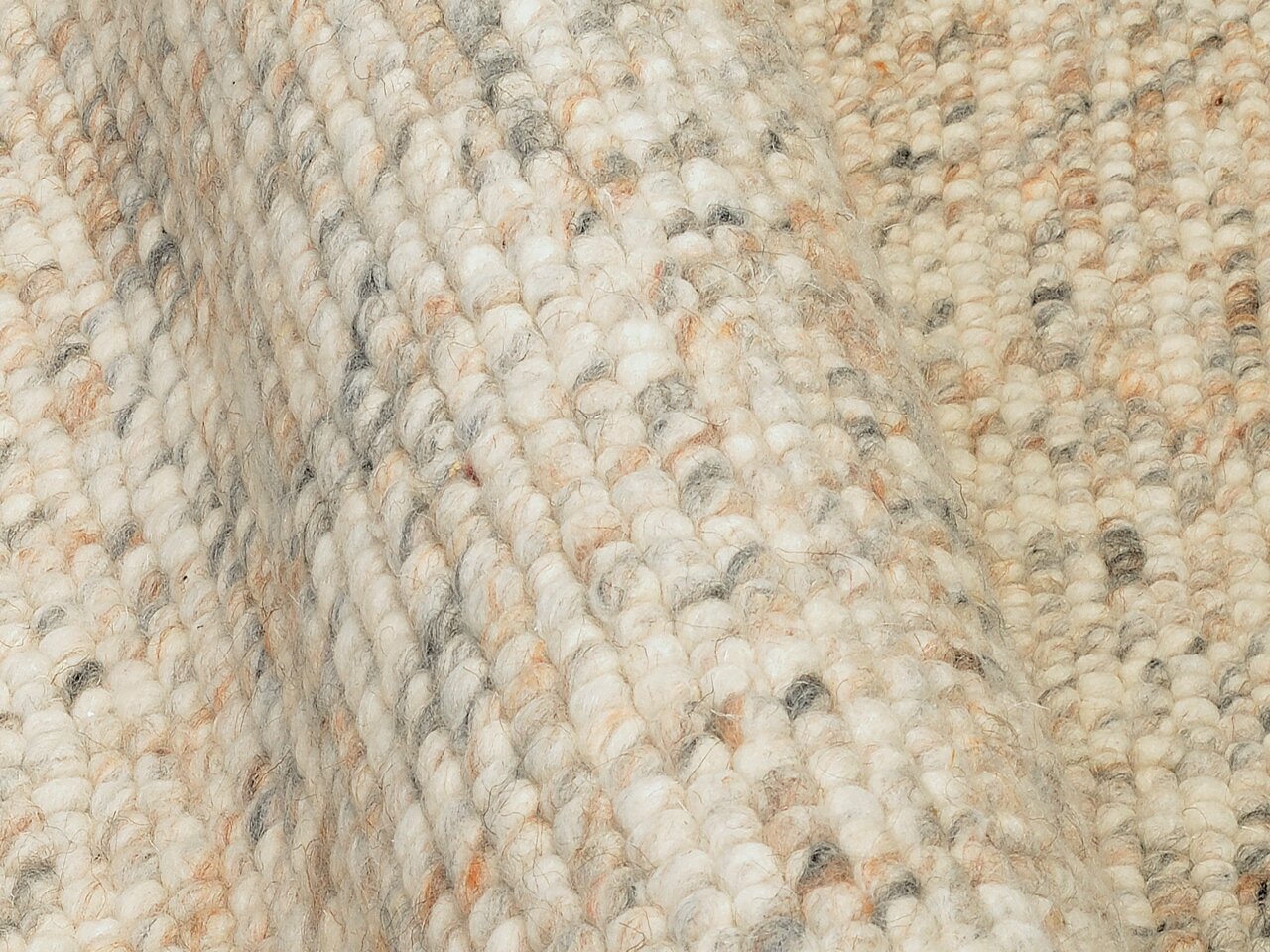 Nahaufnahme eines handgewebten Teppichs mit grober Textur in natürlichen Beige- und Grautönen, seitliche Perspektive.