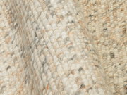 Nahaufnahme eines handgewebten Teppichs mit grober Textur in natürlichen Beige- und Grautönen, seitliche Perspektive.