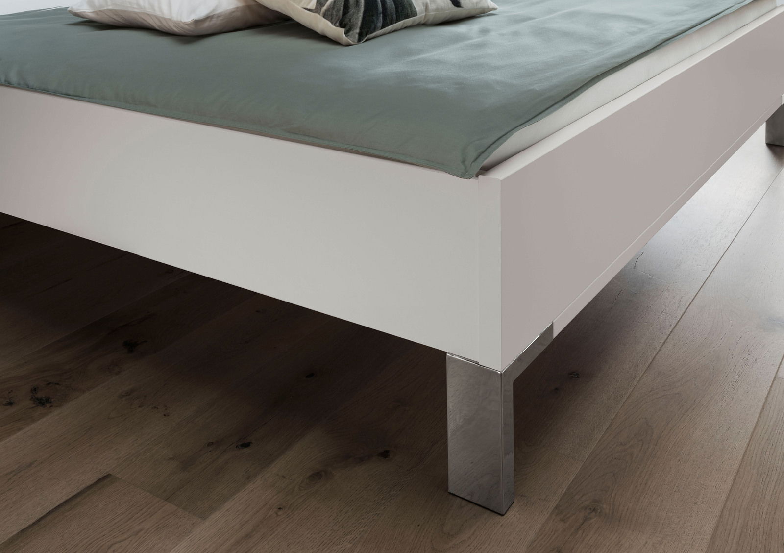 Nahaufnahme eines weißen Futonbetts mit metallischen Beinen, von der Seite fotografiert.