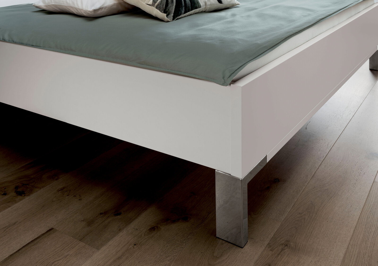 Nahaufnahme eines weißen Futonbetts mit metallischen Beinen, von der Seite fotografiert.