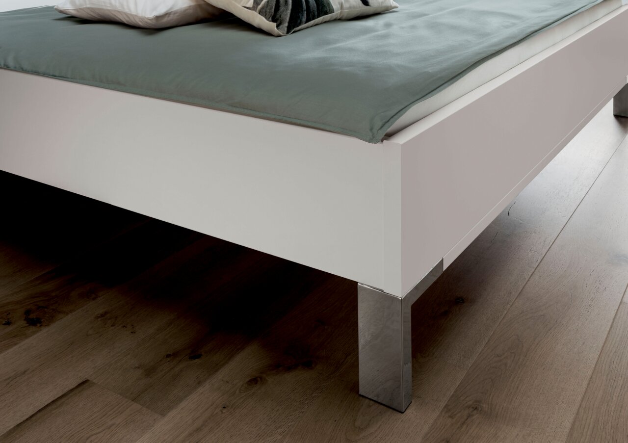 Nahaufnahme eines weißen Futonbetts mit metallischen Beinen, von der Seite fotografiert.