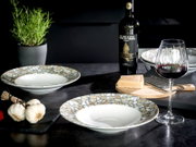 Modernes Tisch-Arrangement mit zwei tiefen Keramikschalen im Mosaik-Design, Rotweinglas, Weinflasche, Parmesan auf Holzbrett mit Reibe, Knoblauch und Kräutertopf auf dunkler Arbeitsplatte, fotografiert aus leicht erhöhter Frontperspektive.